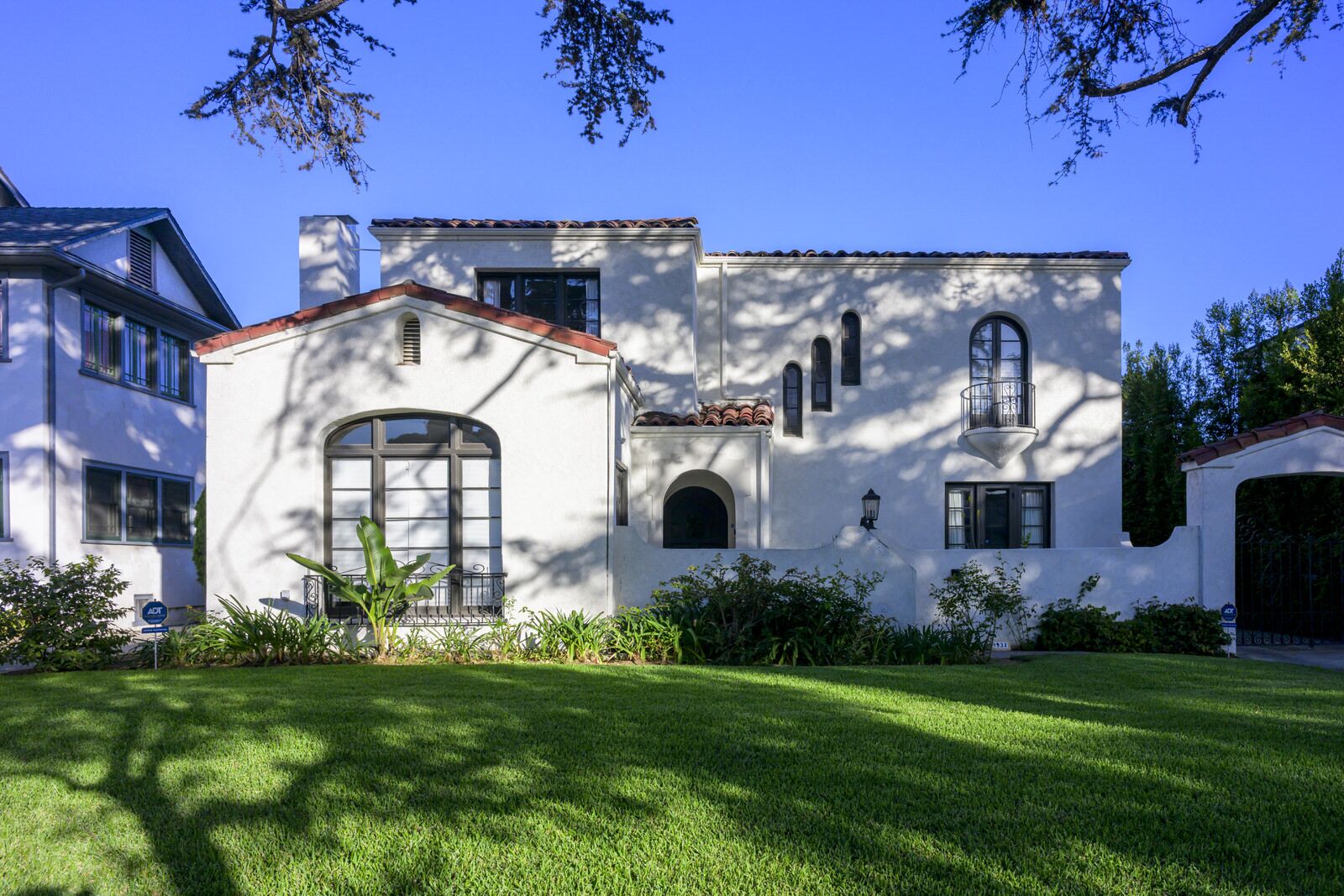 A white Spanish Colonial Revival home with a tall arched window and red tile accents