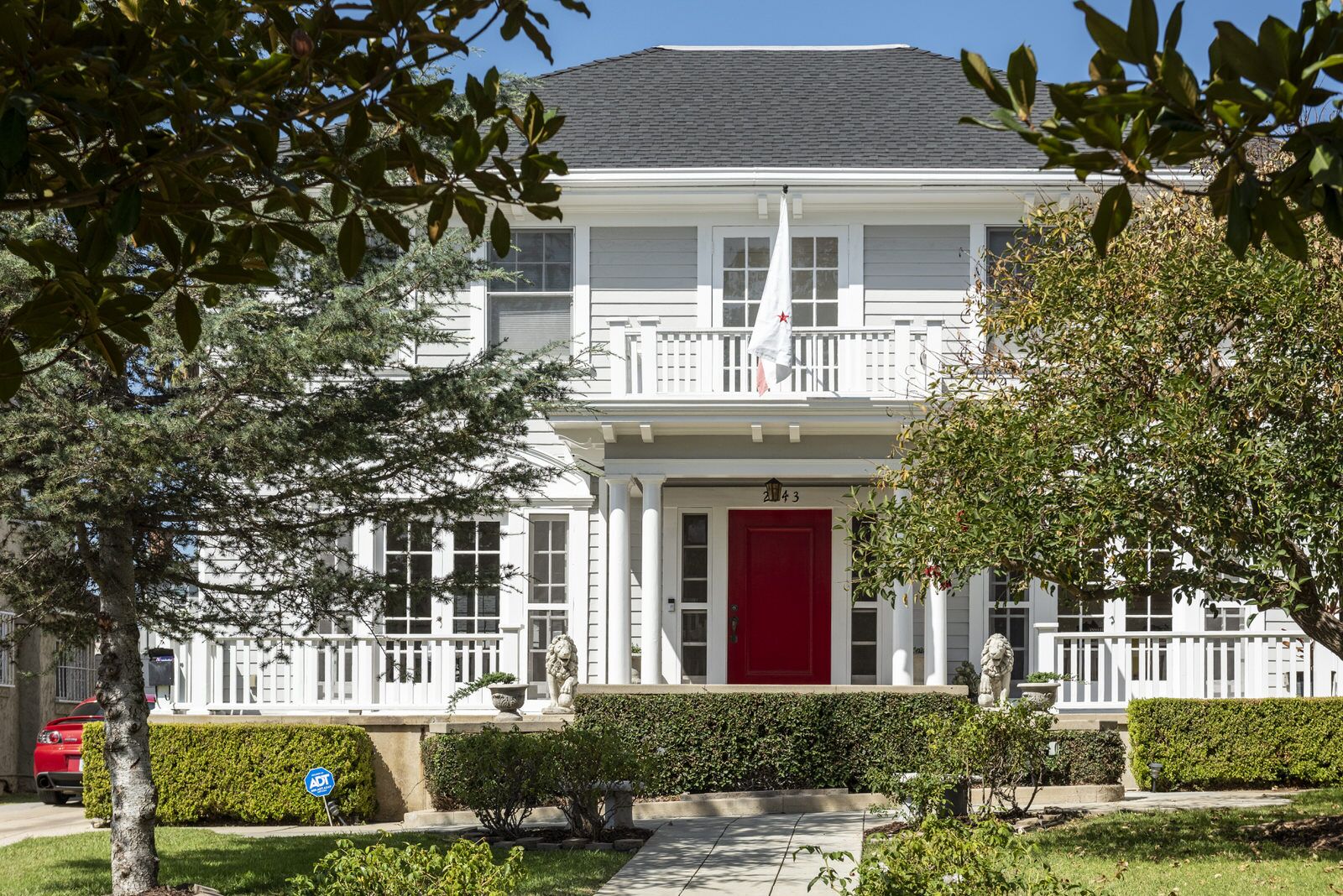 A white Colonial Revival home with a columned porch, balcony, and red front door