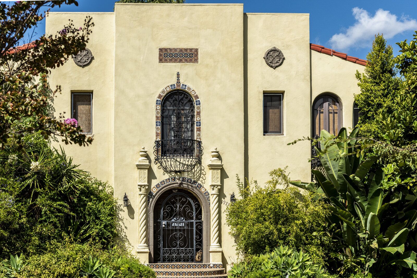 A cream Mediterranean Revival facade with an ornate arched entry and wrought-iron balcony