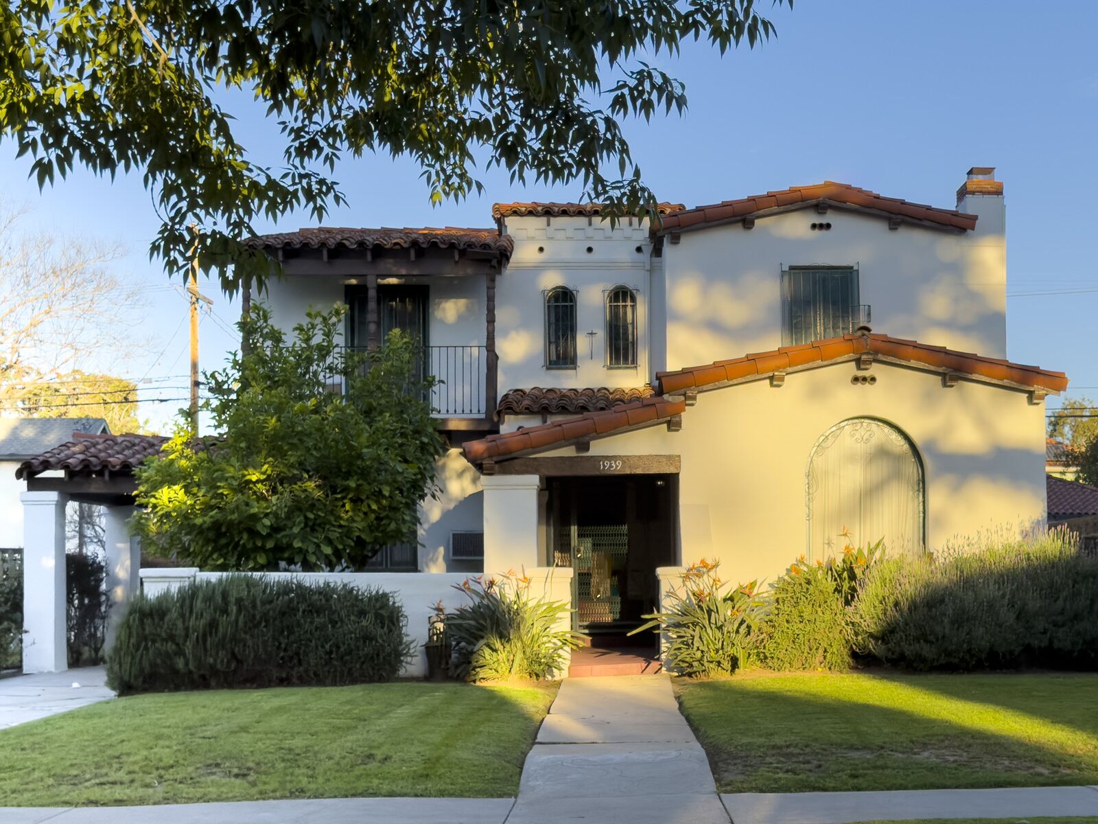 A two-story Spanish Revival home with a red tile roof and garden walk