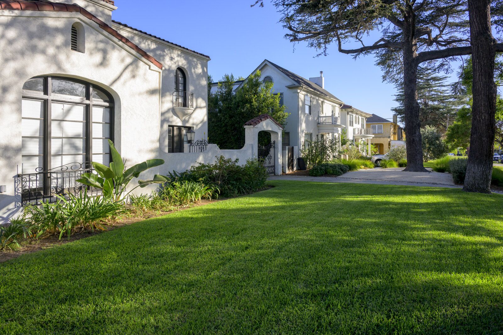 A white Spanish Colonial Revival home with an arched window and a wide green lawn on a sunny Wellington Square street